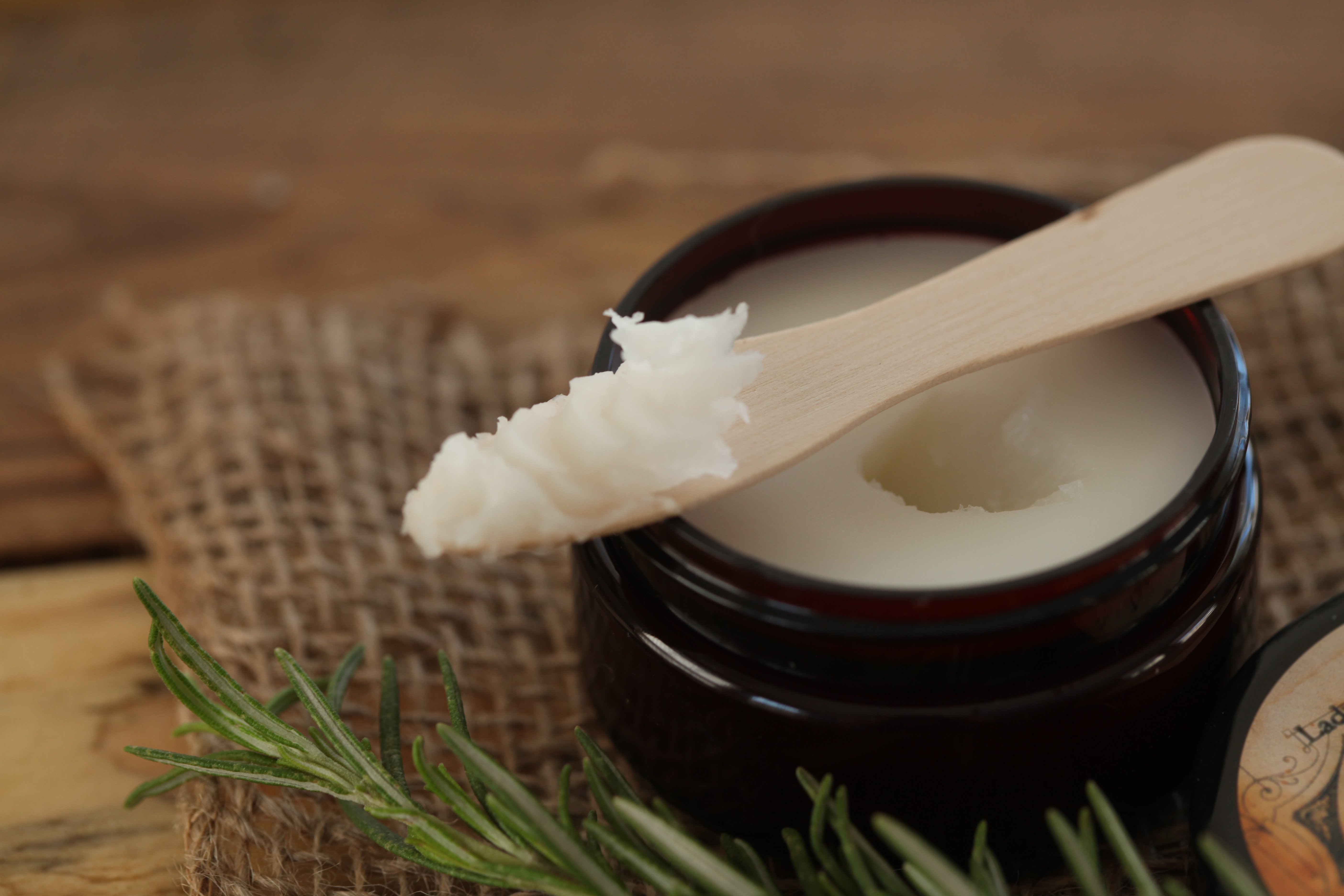 Jar of herbal salve or balm with wooden spoon, on burlap with lavender and rosemary for natural beauty.